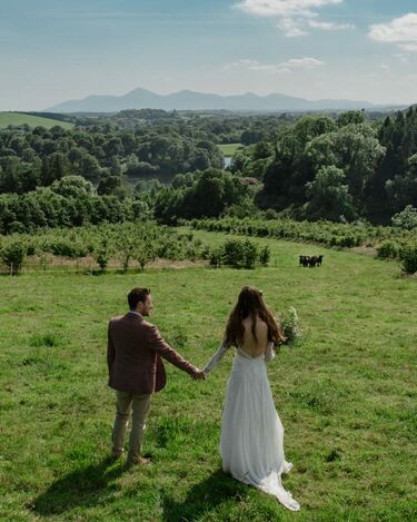 A bride & groom hold hands at the top of a hill overlooking the beautiful Northern Irish countryside