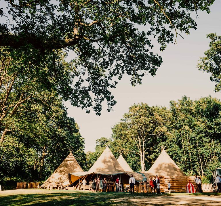 Wedding guests celebrate on a beautiful summers day in our four tipi wedding venue amongst the trees at Finnebrogue Woods