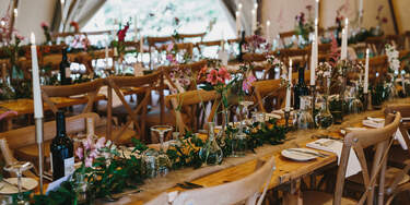 Wildflower and candlesticks arranged on long wooden tables with crossback chairs inside the Tipis at Finnebrogue Woods