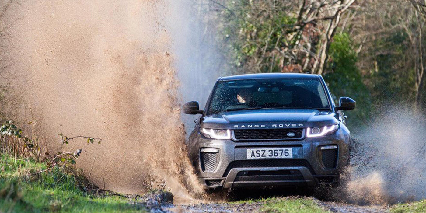 A black Range Rover drives along a trail at Finnebrogue Woods, puddles splash on either side of it