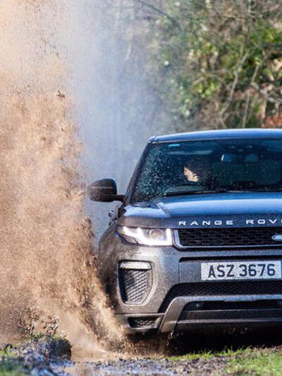 A black Range Rover drives along a trail at Finnebrogue Woods, puddles splash on either side of it