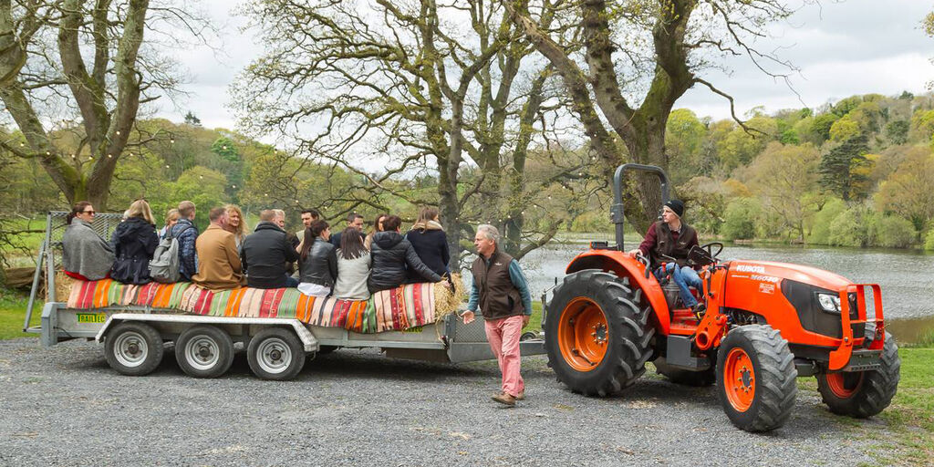 Guests sit on a trailer with hay bales being pulled by a tractor