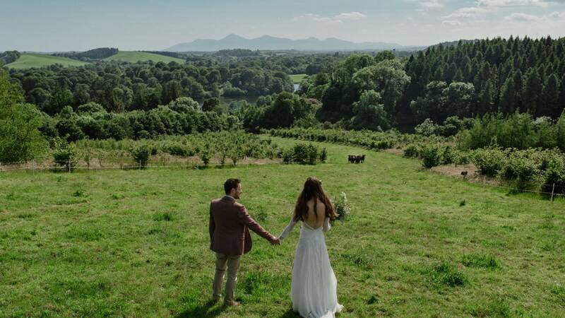 A bride & groom hold hands at the top of a hill overlooking the beautiful Northern Irish countryside