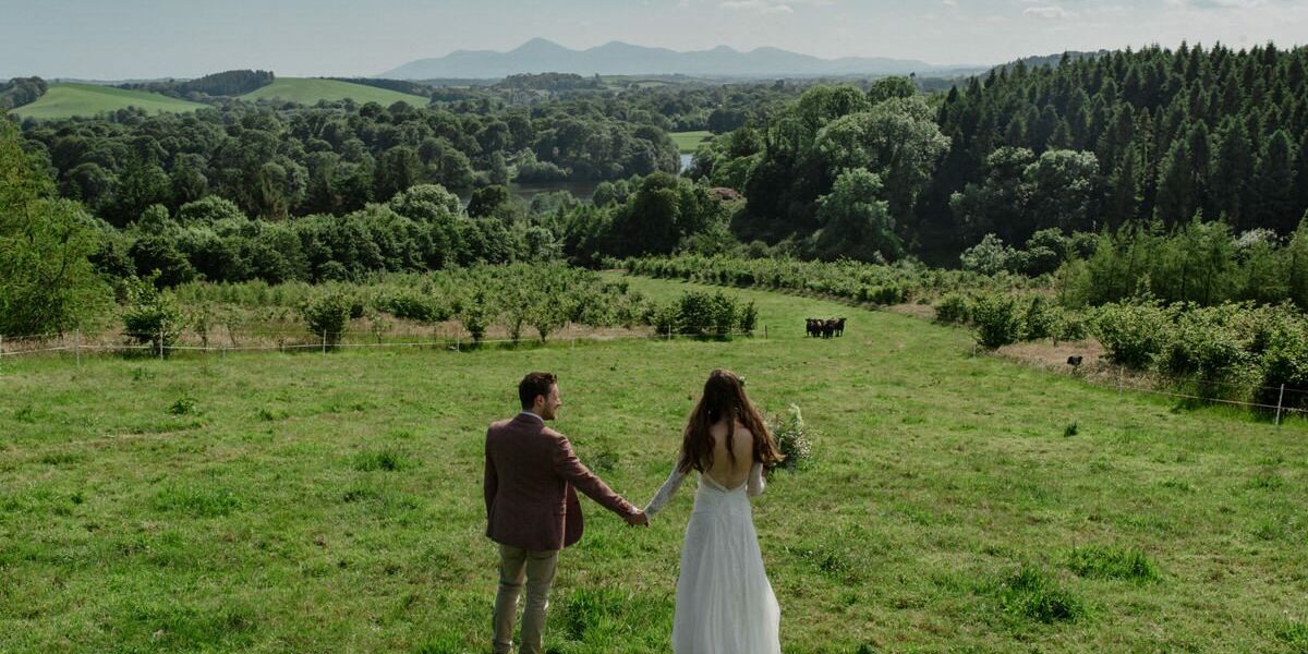 A bride & groom hold hands at the top of a hill overlooking the beautiful Northern Irish countryside