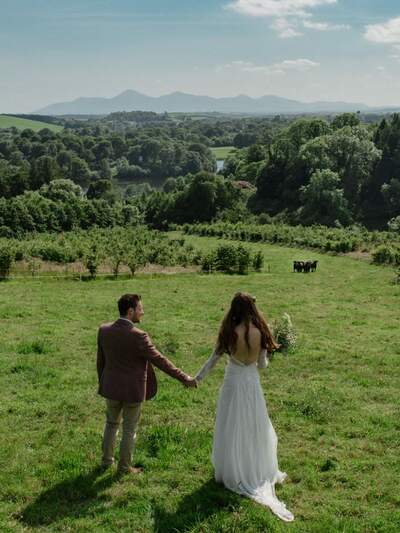 A bride & groom hold hands at the top of a hill overlooking the beautiful Northern Irish countryside