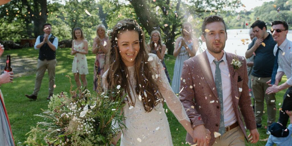 A bride & groom hold hands and smile as they walk through confetti & guests at Finnebrogue Woods