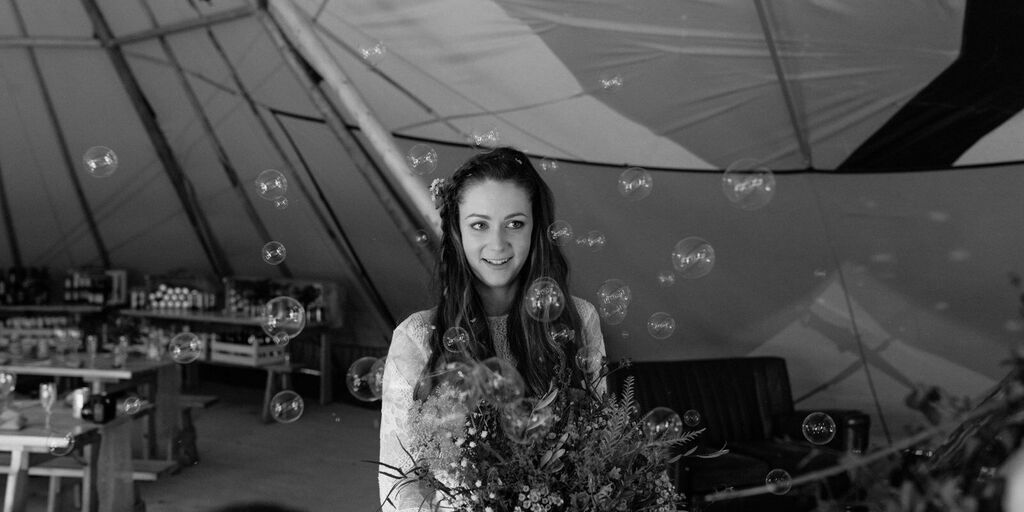 A bride holds her bouquet as she stands inside a Tipi