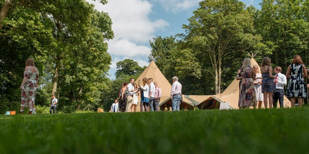 Guests gather in groups at Finnebrogue Woods outdoor Tipi wedding venue surrounded by woods