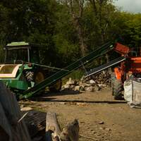 A machine and a tractor are in the woodyard, where prepping our seasoned hardwood for sale takes place