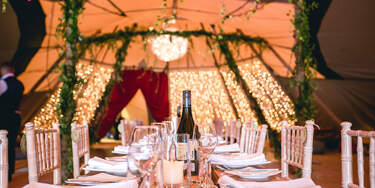 Inside the Tipis at Finnebrogue Woods decorated with green foliage, three panels of fairy lights and a giant orb chandelier