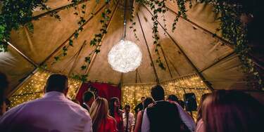 A Giant orb chandelier hangs from the roof of a Tipi and wedding guests party on the dancefloor