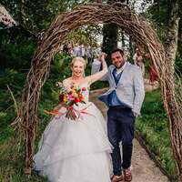 Bride and grom hold hands as they walk through a wicker arch celebrating their wedding day at Finnebrogue Woods