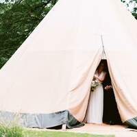 The bride peeks out behind the opening to the bridal tipi at Finnebrogue Woods wedding ceremony site