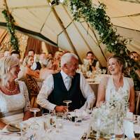 Bride & guests laugh and drink during a wedding reception held inside a tipi venue
