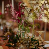 Wildflowers sit in small glass holders on a wooden table, fairy lights decorate the Tipis behind them