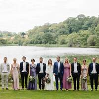 Wedding party & guests stand together in front of Finnebrogue Lake at the tipi venue