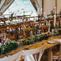 Wildflower and candlesticks decorate  long wooden tables with crossback chairs inside the Tipis at Finnebrogue Woods