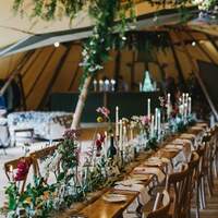 Wedding venue is decorated with wildflowers in a rustic style, long wooden tables & beams dressed in foliage