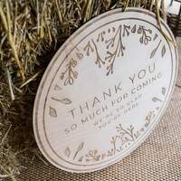 A round rustic wooden sign is carved with a welcome and thank you sign for wedding guests