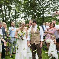 Guests throw dried leaf confetti over the newly married couple as they walk down the aisle