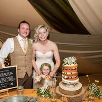 Bride & groom stand beside their wedding cake with a flowergirl inside their Tipi Wedding