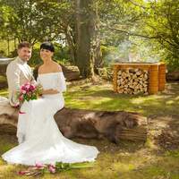 Bride & groom sit on a log with an open firepit beside them