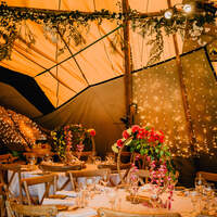 A Tipi is decorated with bright flower centrepieces and round tables at Finnebrogue Woods wedding venue