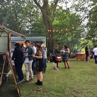 Corporate guests queue for food at a stand amongst the woods at a staff summer party