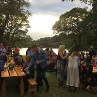 Guests sit outside at picnic benches overlooking Finnebrogue Lake at a corporate summer party