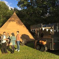 Corporate guests stand outside in front of  tipi venue, a coffee horsebox stands beside it