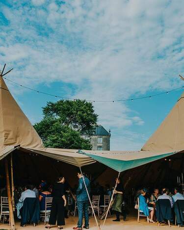 Open sided entrance to a tipi wedding reception, inside is crowded with guests sitting at tables