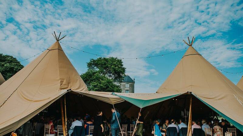 Open sided entrance to a tipi wedding reception, inside is crowded with guests sitting at tables